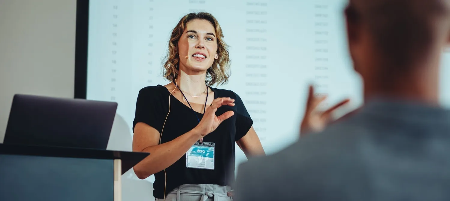 Dozentin steht während eines Bildungsurlaubes vor einer Leinwand und blickt in Richtung der Teilnehmenden